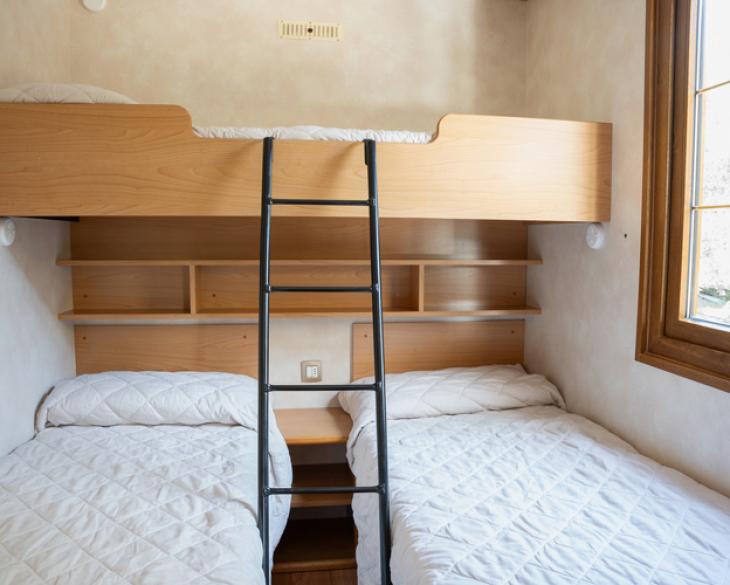 Chambre avec lits superposés, deux lits simples et échelle.