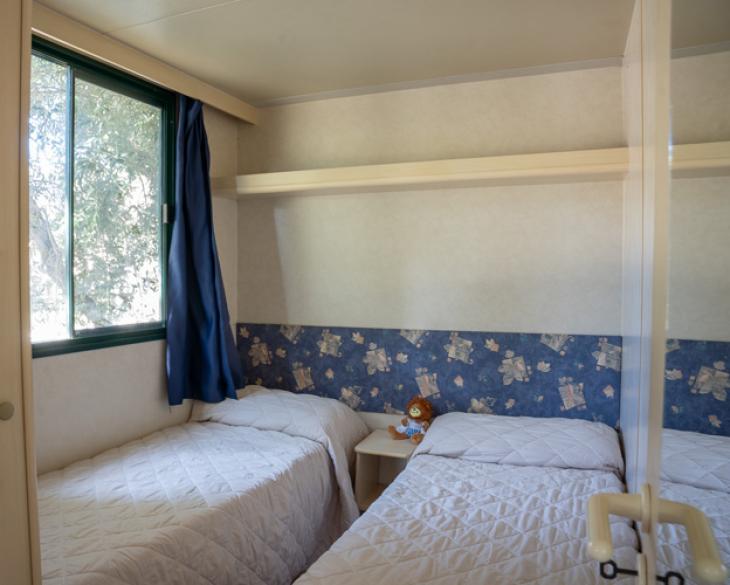 Chambre avec deux lits simples, fenêtre et décorations bleues.