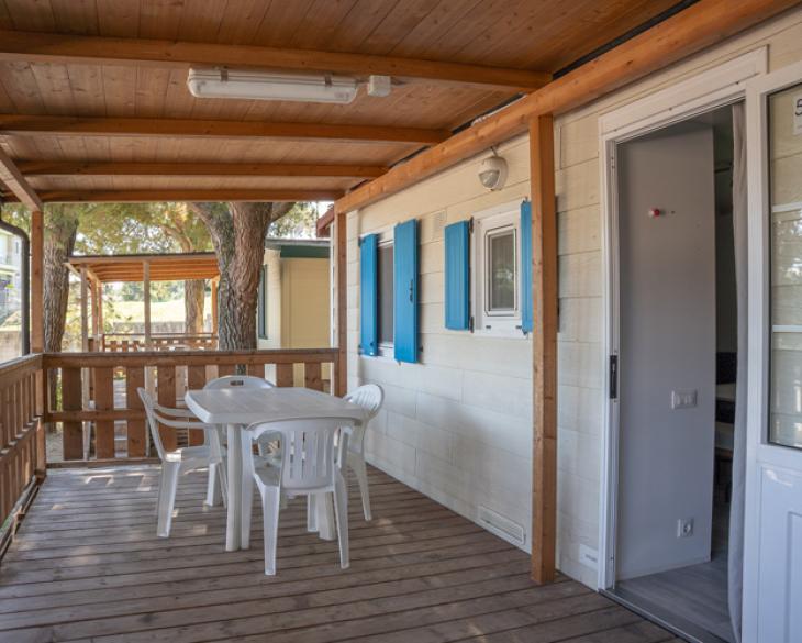 Véranda en bois avec table et chaises blanches, à côté d'une maison mobile.
