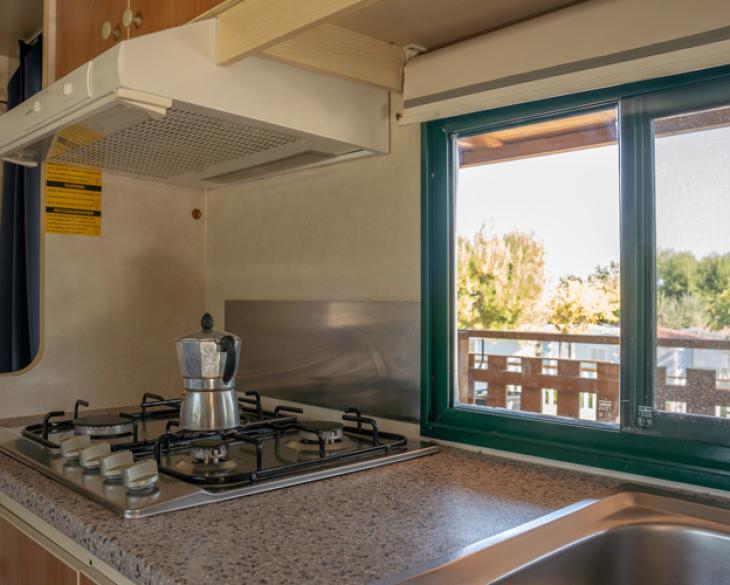 Cuisine avec cuisinière à gaz et cafetière, vue sur le balcon.