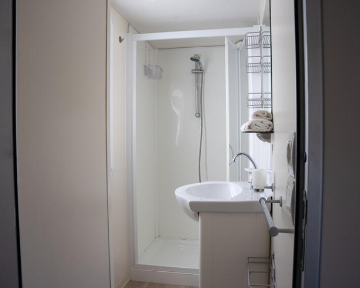 Salle de bain moderne avec douche, lavabo et étagères blanches.