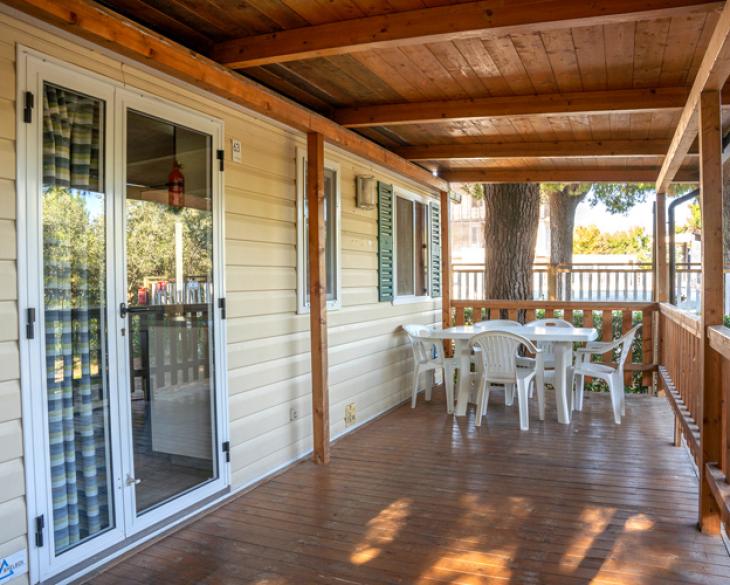 Véranda en bois avec table et chaises blanches, entourée de verdure.