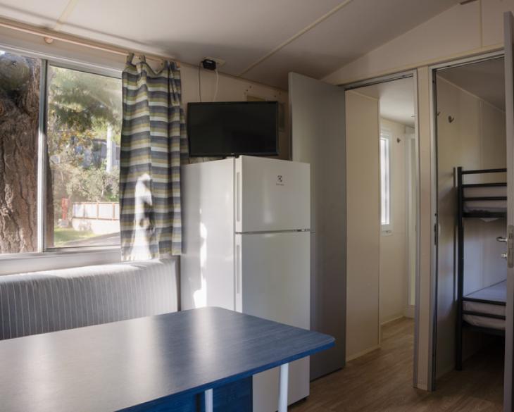 Intérieur de maison mobile avec table, frigo et lits superposés.