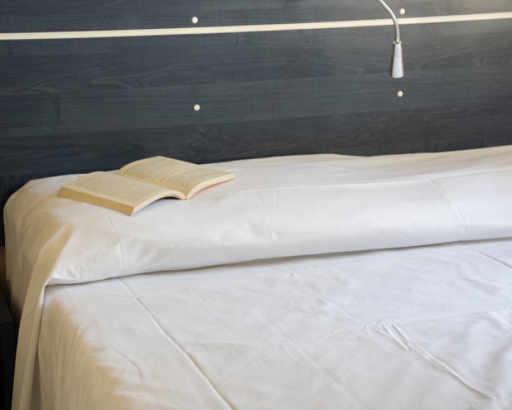 Lit avec draps blancs et livre ouvert.