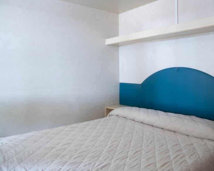 Chambre simple avec lit double et tête de lit bleue.