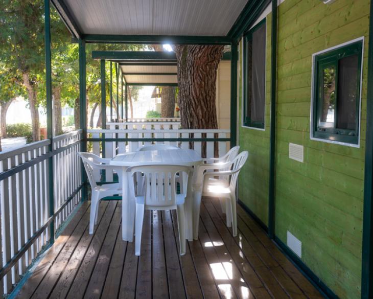 Véranda avec table et chaises en plastique, entourée de verdure.