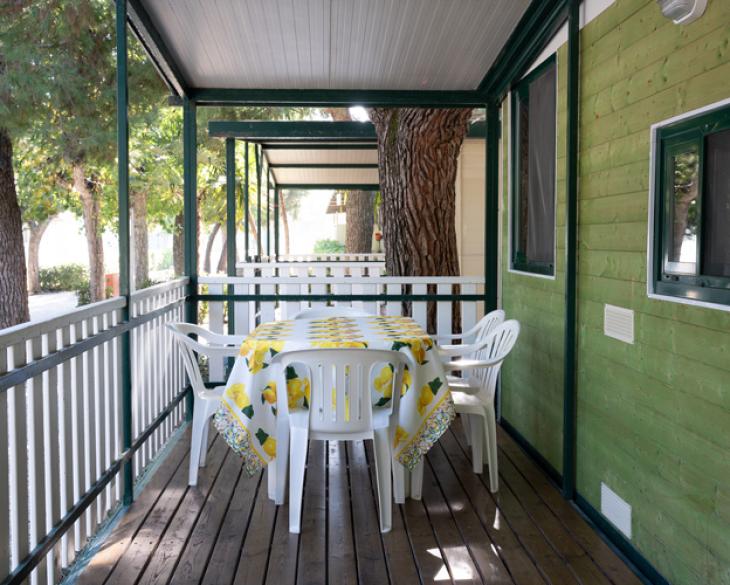 Véranda avec table et chaises blanches, entourée d'arbres.