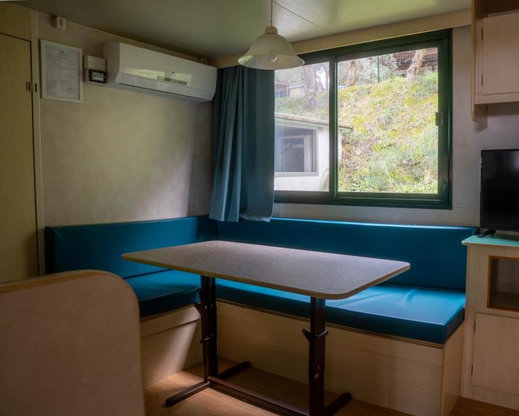 Intérieur de maison mobile avec table, canapé, TV et fenêtre.